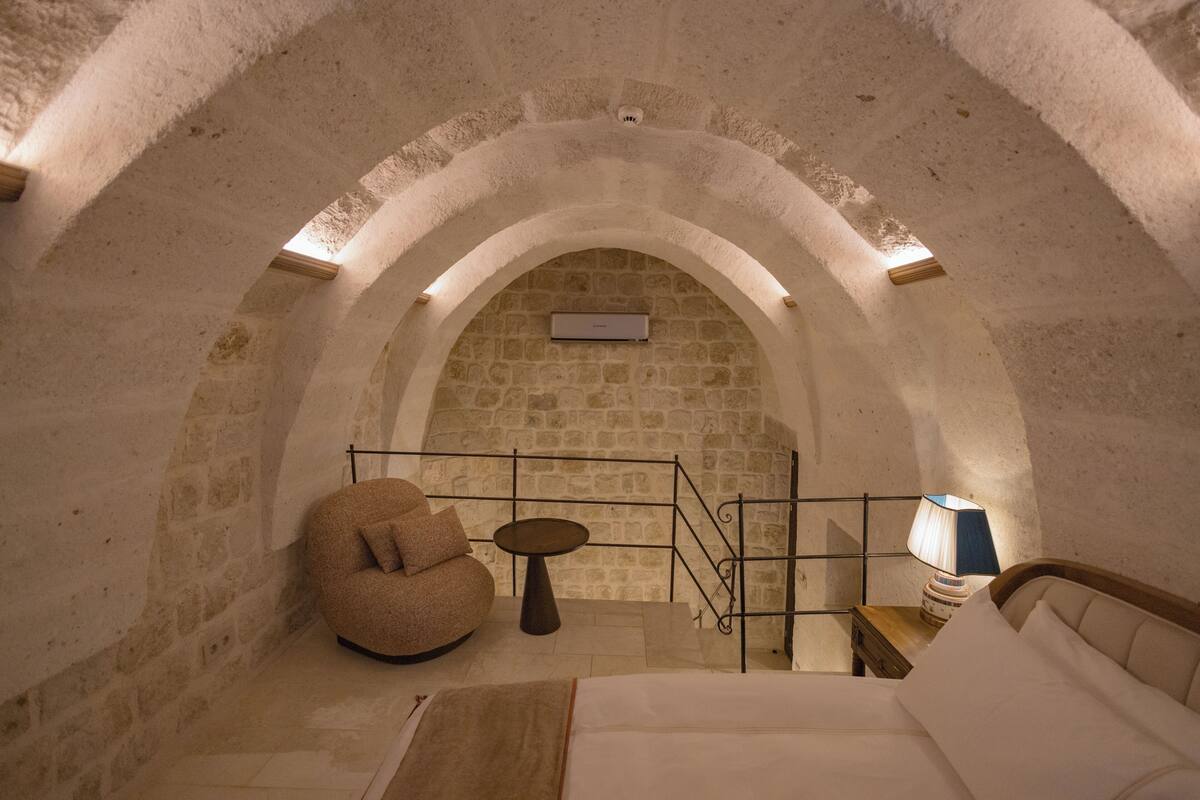 A cozy room with a stone wall, a round seating area, a bed, and a small table with a lamp.