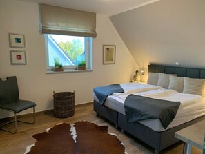 A bedroom with a bed, a chair, a window with plants, a statue, and a cowhide rug. - Haus Seeblick Modern Retreat (Goehren-Lebbin)