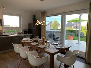 A modern dining area with a wooden table set for six, white chairs, and a view of the backyard through large sliding glass doors. - Haus Seeblick Modern Retreat (Goehren-Lebbin)