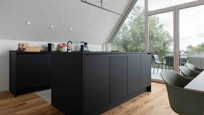 A modern kitchen with a large island, wooden flooring, and a view of the outdoors through large windows. - Harlepadd 3c Modern Retreat (Wittmund)