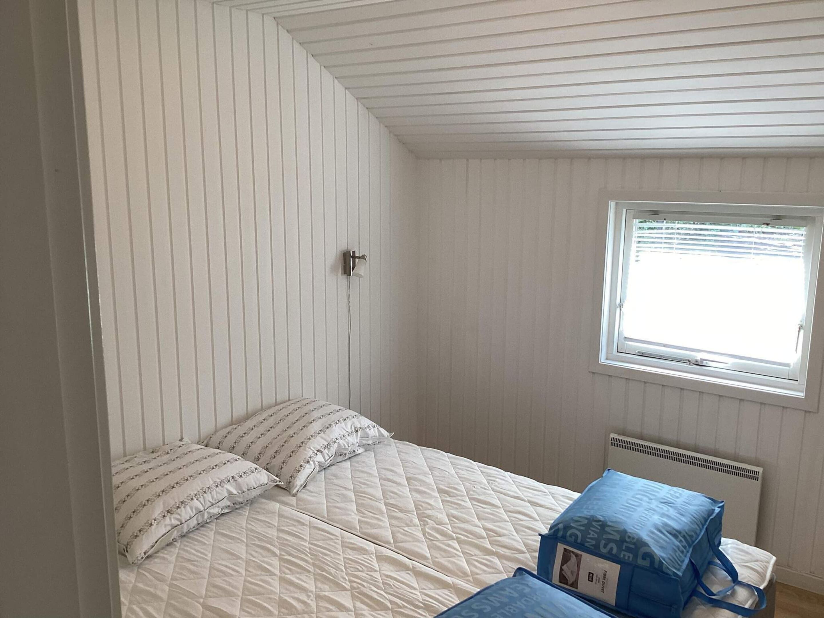 A small, single-bed room with a sloped ceiling, a window with blinds, and a radiator.