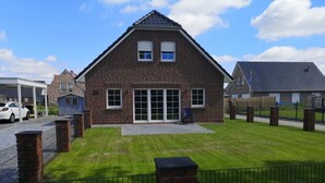 A two-story brick house with a sloped roof, a covered patio, and a fenced yard. - Dat Ankerhuus Timmel (Grosefehn)
