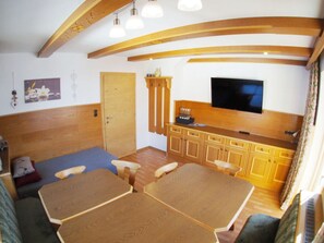 A compact living space with a wooden ceiling, a television mounted above a wooden cabinet, and a dining table with four chairs. - Vakantiehuis Sonneck (Hainzenberg)