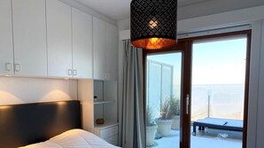 A bedroom with a bed, white cabinets, a sliding glass door to a balcony, and a hanging light fixture. - Attic Apartment Nieuwpoort With Coastal Views (Nieuwpoort)
