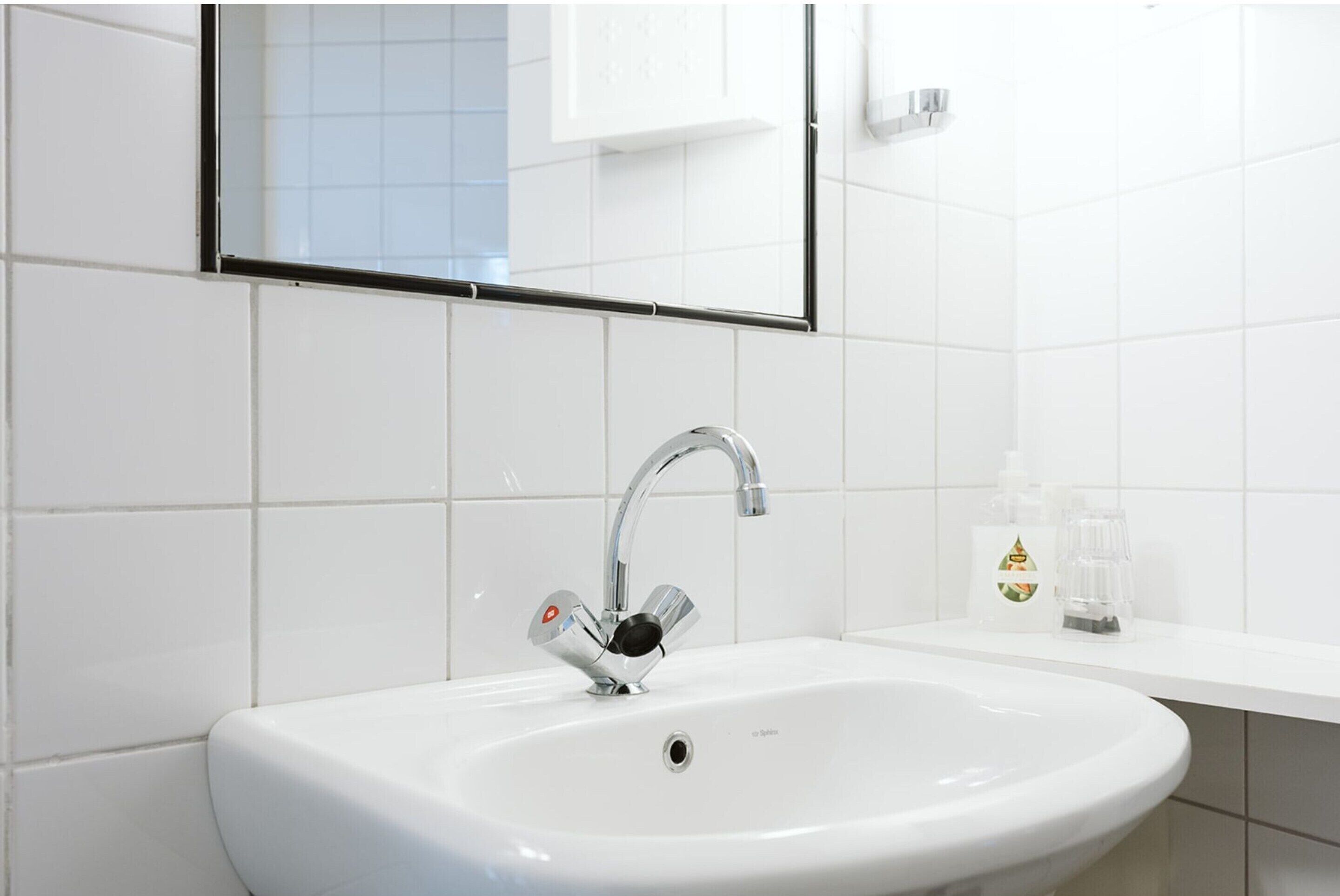 Un lavabo blanc dans une salle de bain, doté d’un robinet moderne, avec un miroir au-dessus et une petite étagère contenant des articles de toilette.