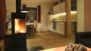 A cozy living room with a wood-burning stove, a dining area, and a kitchen with modern appliances. - Apartment in Eibenstock (Eibenstock)