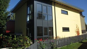 A modern building with a flat roof, large windows, and a wooden fence with flowers. - Apartment in Eibenstock (Eibenstock)
