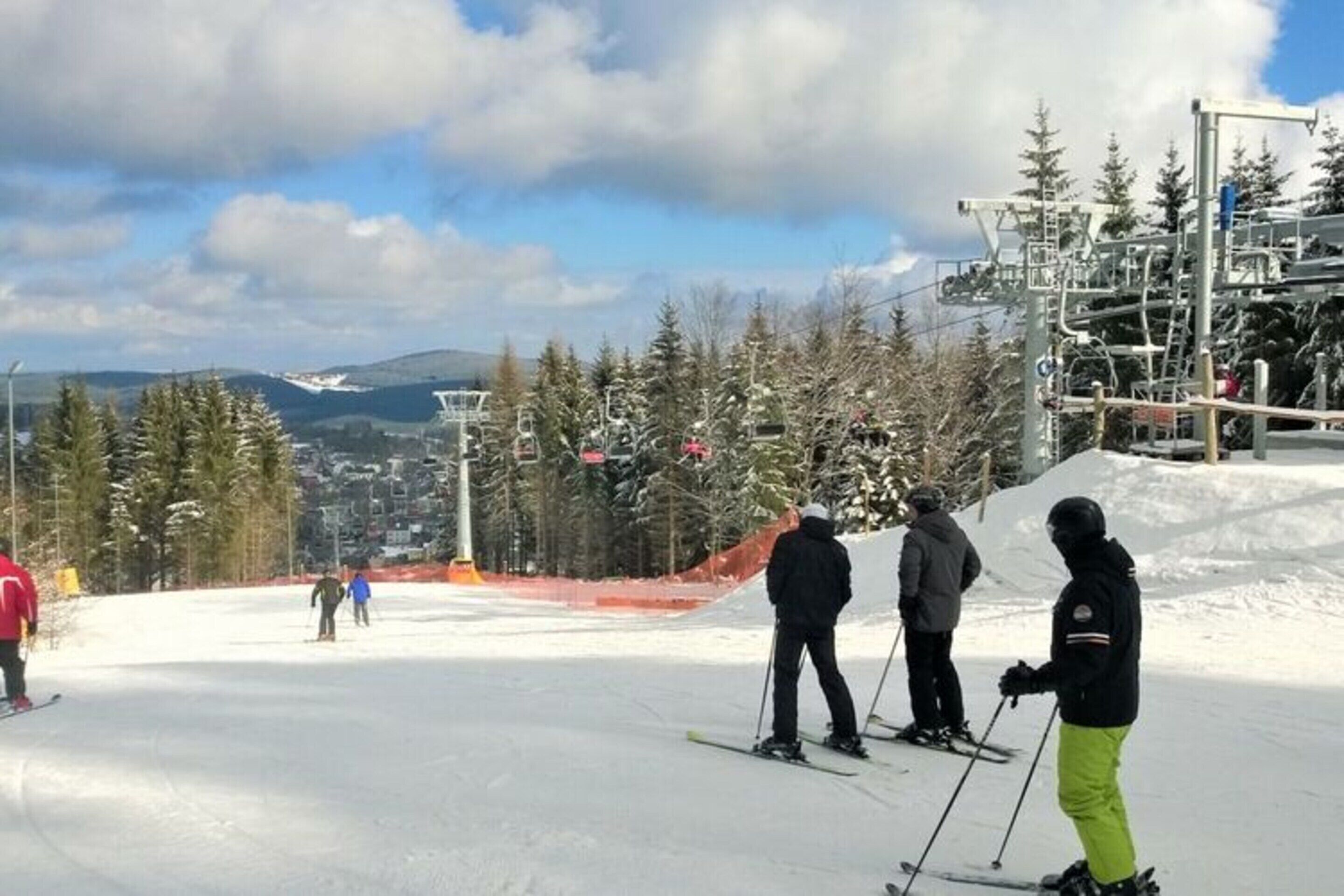 A ski slope with skiers, a ski lift, and a mountainous backdrop.