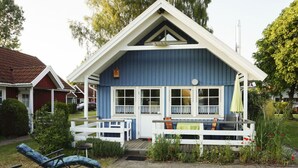 Et blå hus med en hvid veranda, en lille terrasse og en have med planter og blomster.