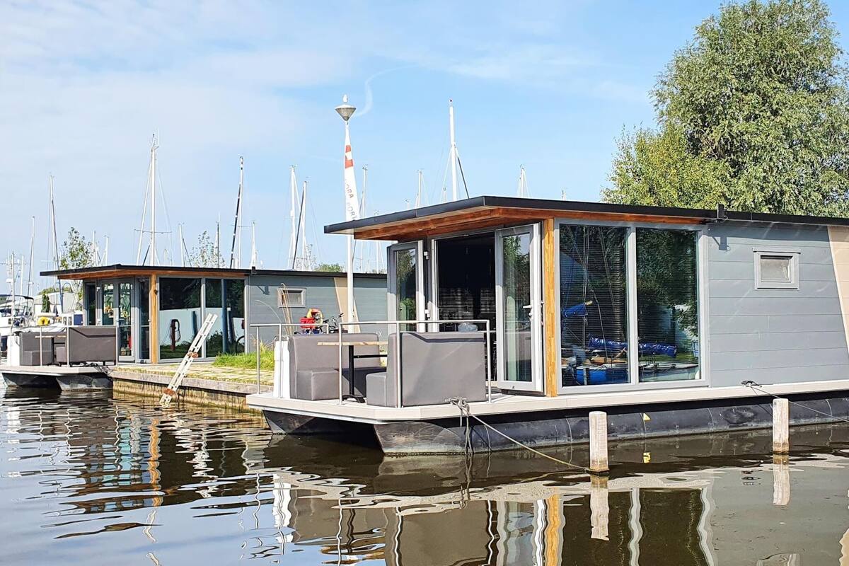 A floating houseboat with a modern design, featuring large glass windows and a wooden deck.