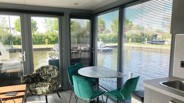 Una habitación moderna con zona de comedor, cocina y vistas a un cuerpo de agua a través de amplios ventanales.