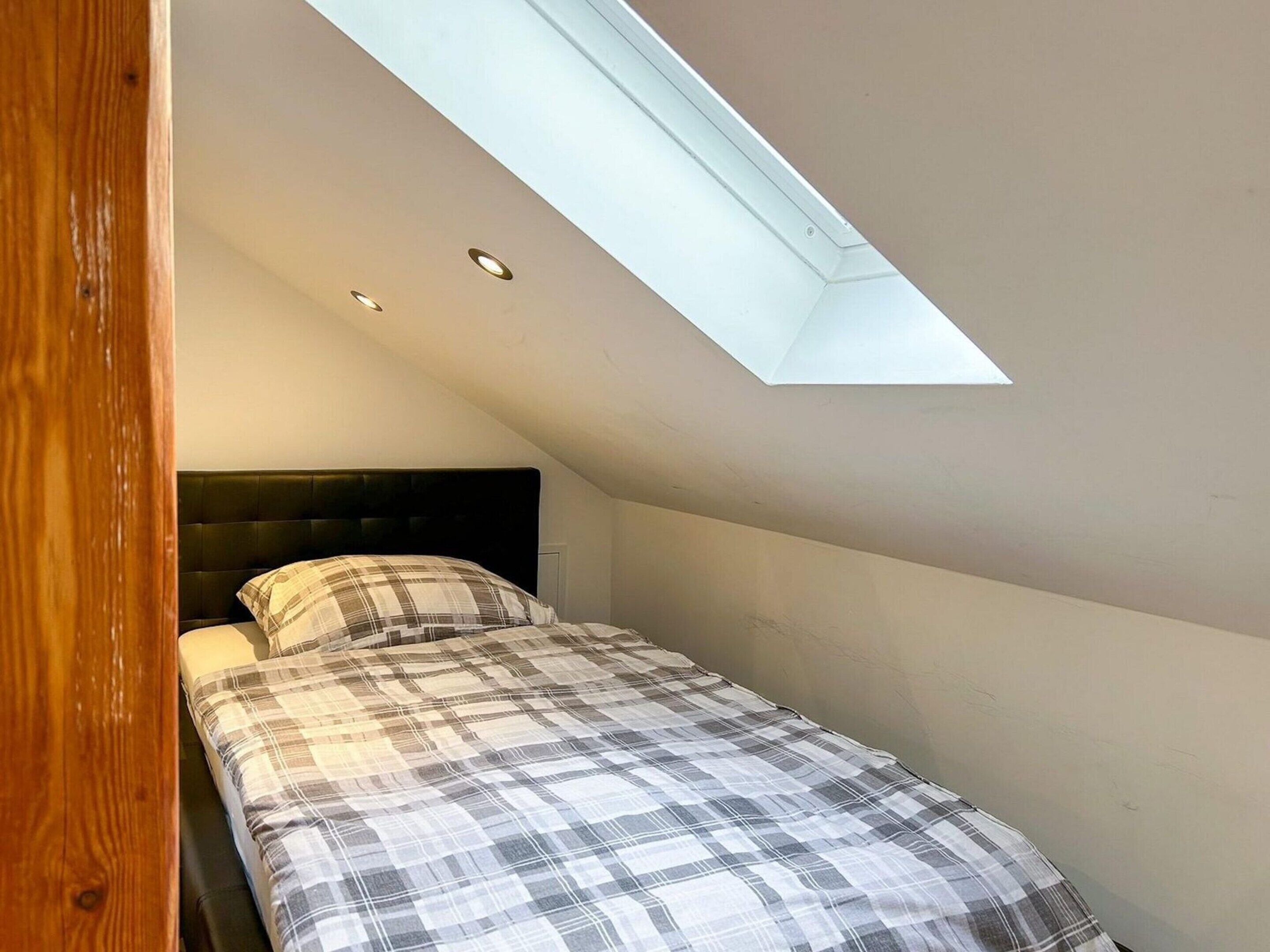 A bedroom with a skylight, a bed with a plaid bedspread, and a dark headboard.