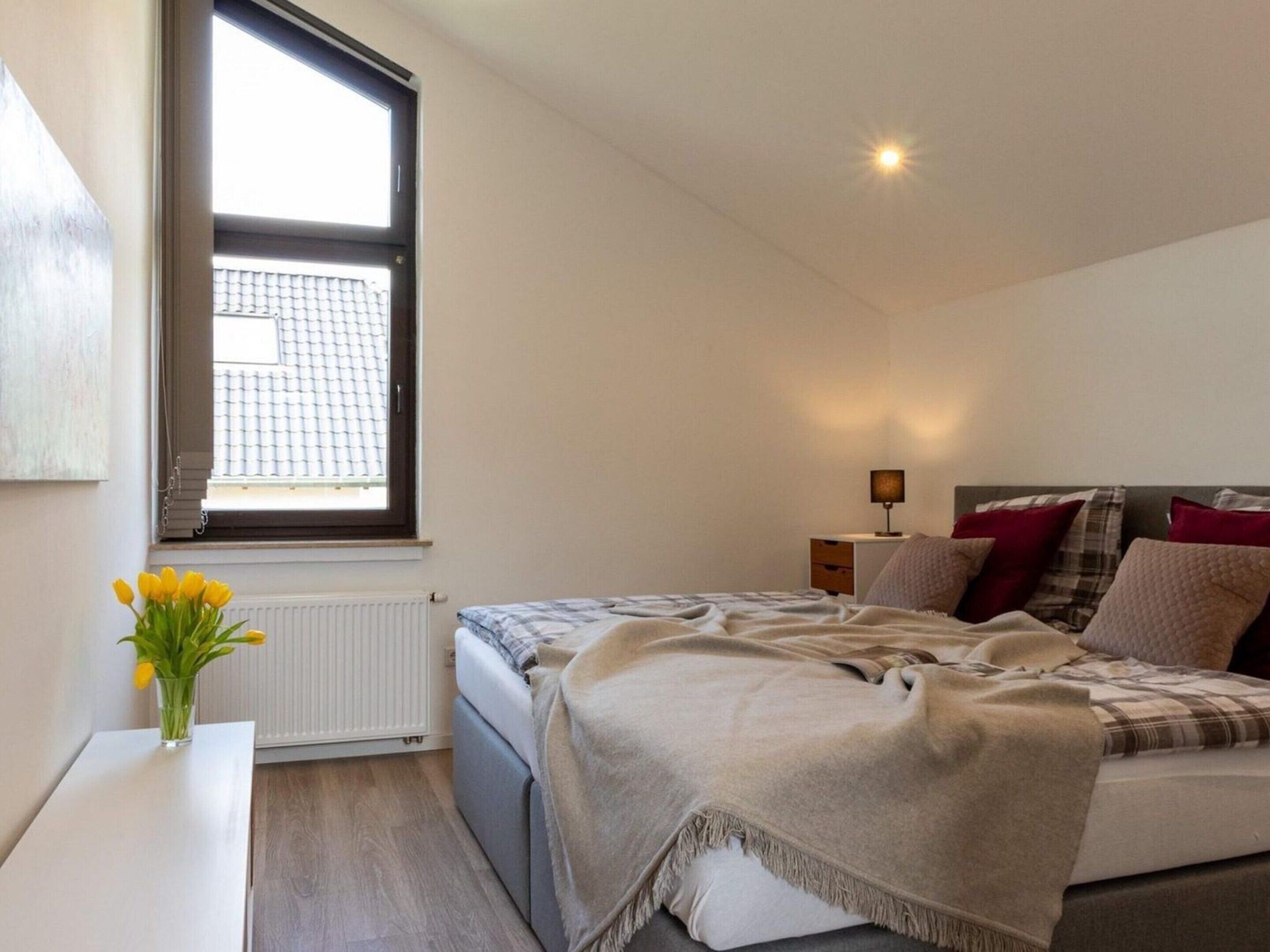 A bedroom with a bed, bedside table, lamp, and a window with a view of a building.