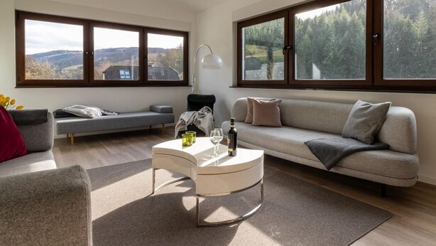 Un salon moderne avec un canapé, une table basse et une vue sur l’extérieur grâce à de grandes fenêtres.