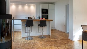Une cuisine moderne avec un parquet en bois disposé en motif chevrons, deux tabourets de bar et un four encastré.