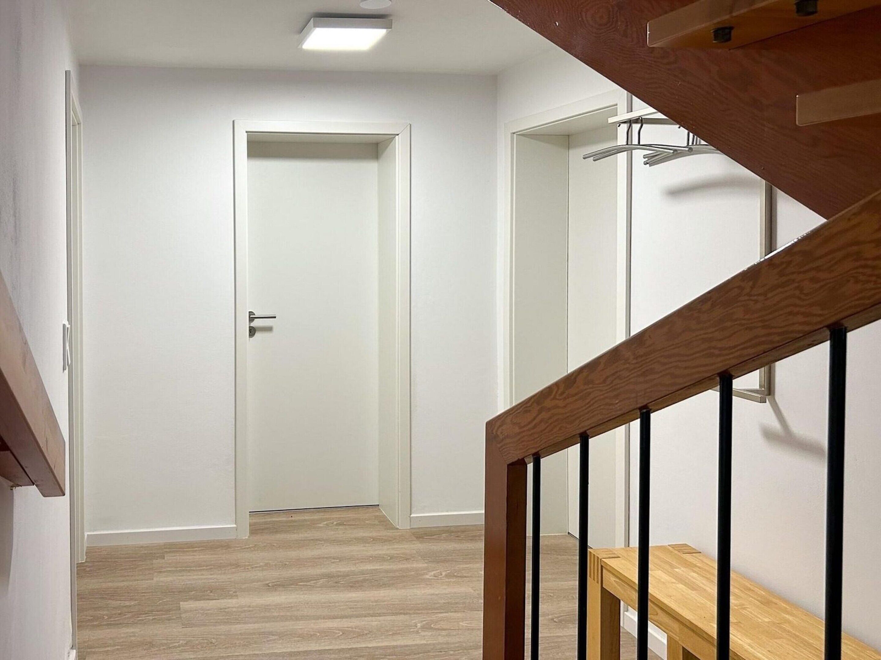 Un couloir avec un escalier en bois, une porte blanche et un porte-manteau.