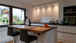 Une cuisine moderne avec un îlot central, deux tabourets de bar, une bouteille de vin, des verres et un panier de fruits.