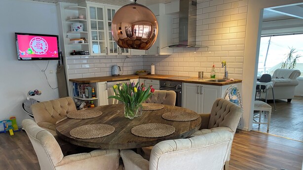 A modern kitchen with white cabinets, a copper pendant light, and a dining area with a round wooden table and cushioned chairs.