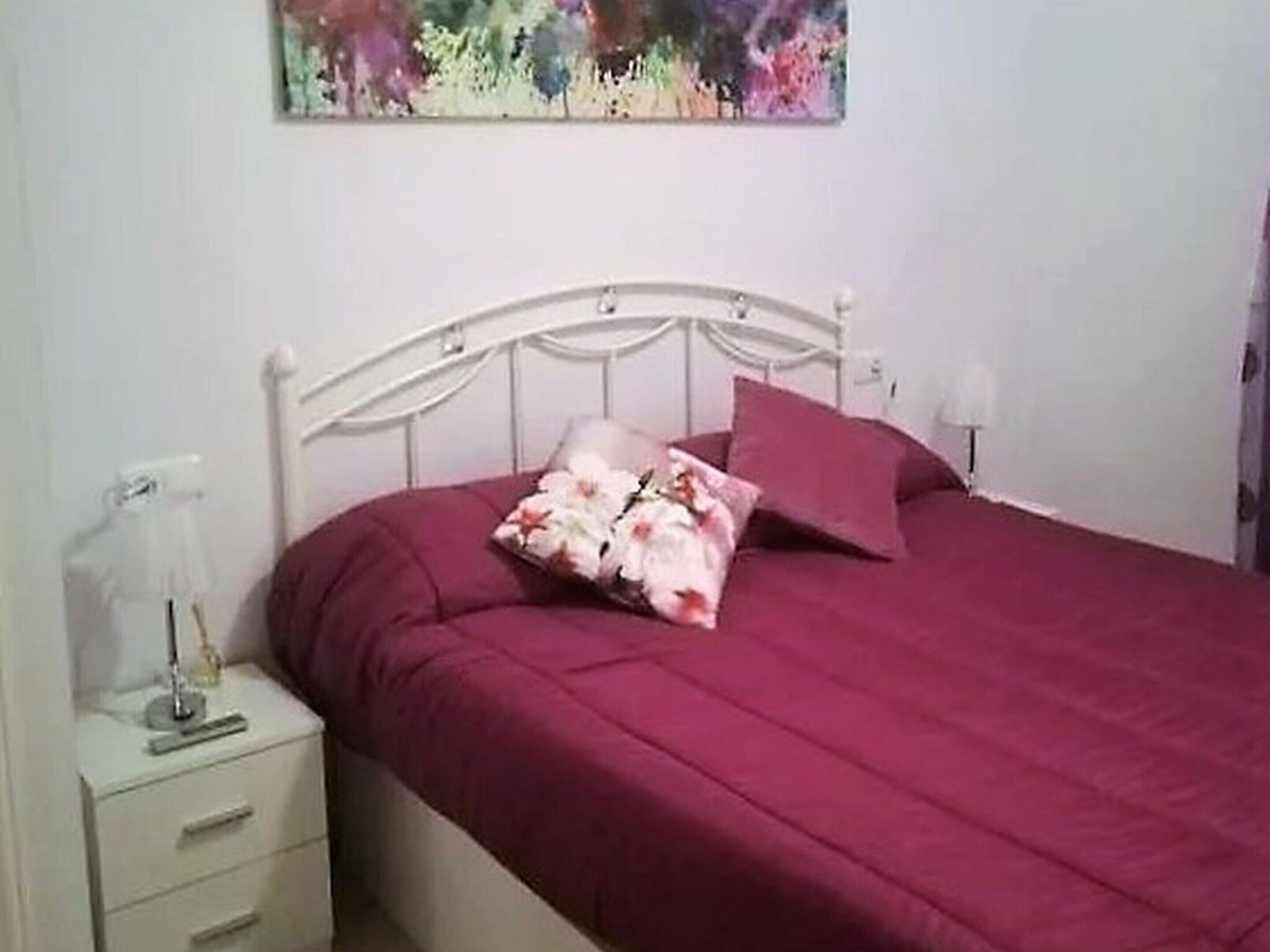 A bed with a white headboard, a red bedspread, and a floral pillow.