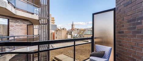 A balcony with a chair, a wooden table, and a metal railing.