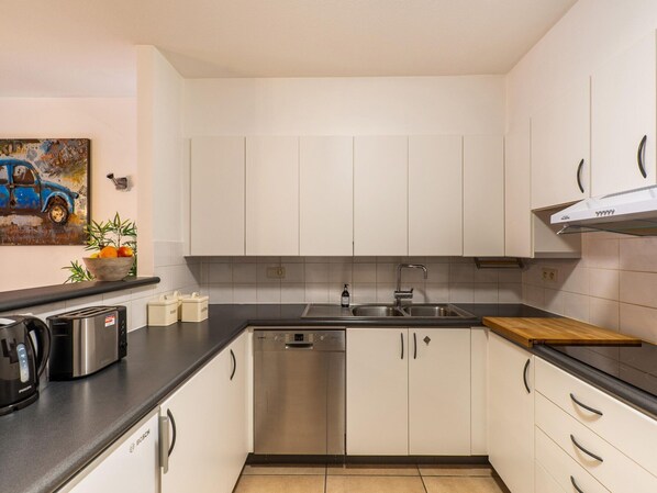 Una cocina moderna con gabinetes blancos, lavavajillas de acero inoxidable y encimera negra.