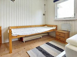 A single bed with a wooden frame and white bedding in a room with wooden flooring, a window, and a small bedside table with a heater. - 5 Person Holiday Home in Karrebaeksminde (Karrebæksminde)