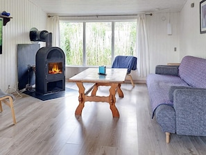 A cozy living room with a fireplace, a sofa, a table, and a view of greenery outside. - 5 Person Holiday Home in Karrebaeksminde (Karrebæksminde)