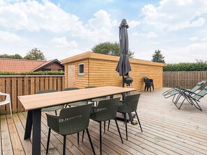 A wooden deck with a table and chairs, a barbecue grill, and a covered umbrella.
