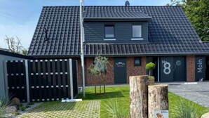 Un bâtiment moderne avec un toit en tuiles, une façade en briques et une entrée fermée par un portail.
