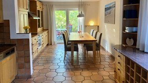 Ett kök med ett sexkantigt kakelgolv, träskåp, ett matbord med stolar och utsikt över grönområden utanför.
