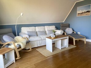 Un salon chaleureux avec un canapé blanc, des coussins à rayures, une table basse en bois et un fauteuil à bascule.