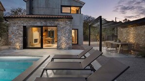Une maison moderne avec une façade en pierre, une piscine et un espace salon extérieur.