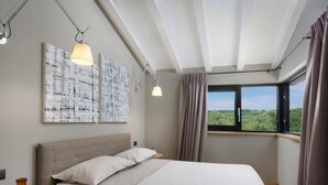 Une chambre à coucher avec un lit, deux lampes fixées au mur, une fenêtre avec des rideaux et deux tableaux abstraits.