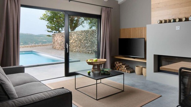 Un salon moderne avec un canapé, une table basse et un téléviseur. On peut voir un mur en pierre et une piscine à travers les portes vitrées.