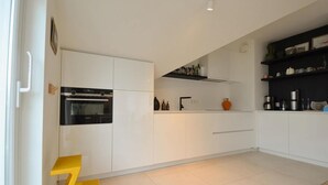 A modern kitchen with white cabinetry, a black oven, a yellow stool, and a black shelf with kitchen items.