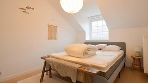 A bedroom with a bed, a hanging light fixture, a window, and a macrame wall hanging.