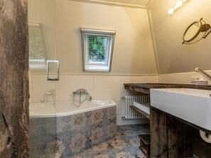 Ein Badezimmer mit Badewanne, Fenster, Spiegel und Waschtisch.