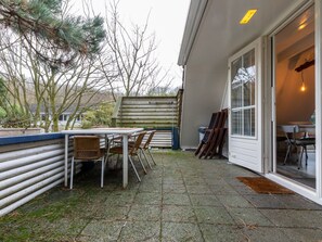 Eine Terrasse mit Tisch und Stühlen, ein Holzzaun und eine Tür zu einem Innenraum.