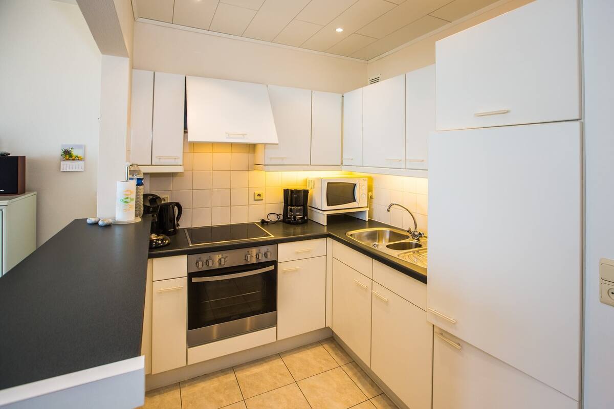 A modern kitchen with white cabinets, a black countertop, stainless steel appliances, and a tiled backsplash.