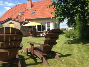 A house with a red-tiled roof, a wooden deck with two Adirondack chairs, a table, and a yellow umbrella. - Holiday Apartment in Gross Schwansee (Kalkhorst)