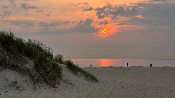 En strand med klitter og en solnedgang over vandet.