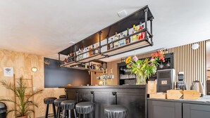 Et moderne barområde med en træbar, sorte barstole, en hylde med flasker og en dekorativ vase med blomster.