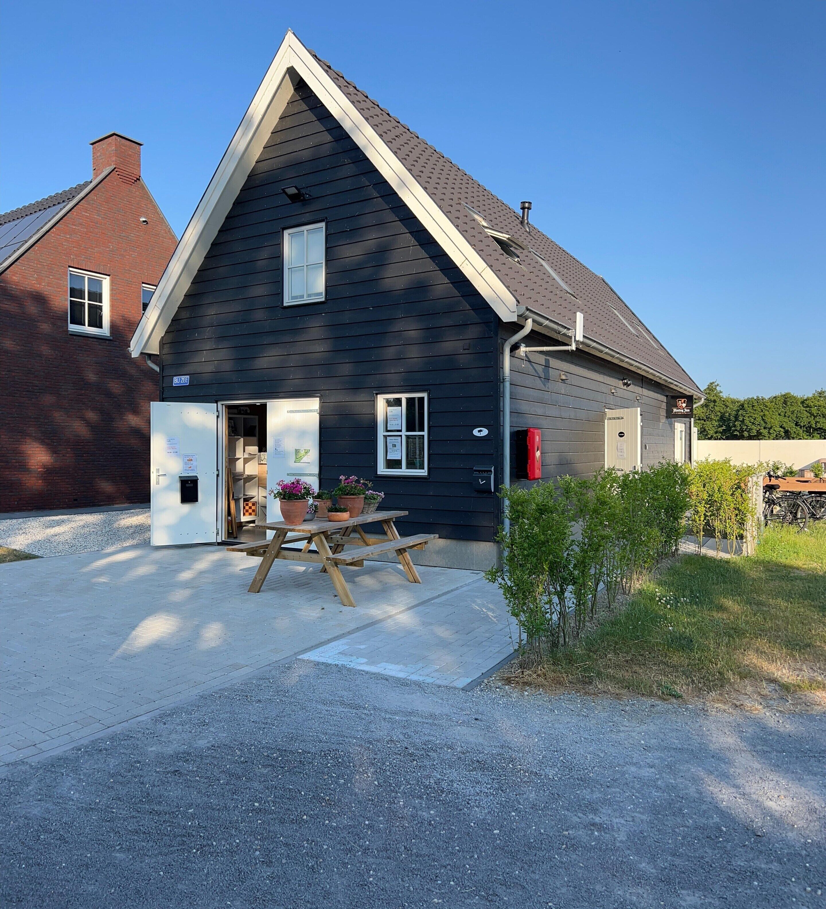 A two-story house with a dark exterior, a visible chimney, and a small front porch with a table and potted plants.