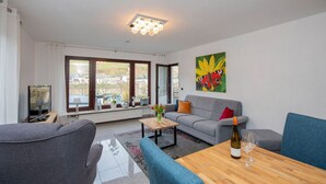 A modern living room with a grey sofa, blue armchairs, a wooden coffee table, and a painting of a butterfly on the wall. - Tranquil Apartment in Zell-kaimt (Zell (Mosel))