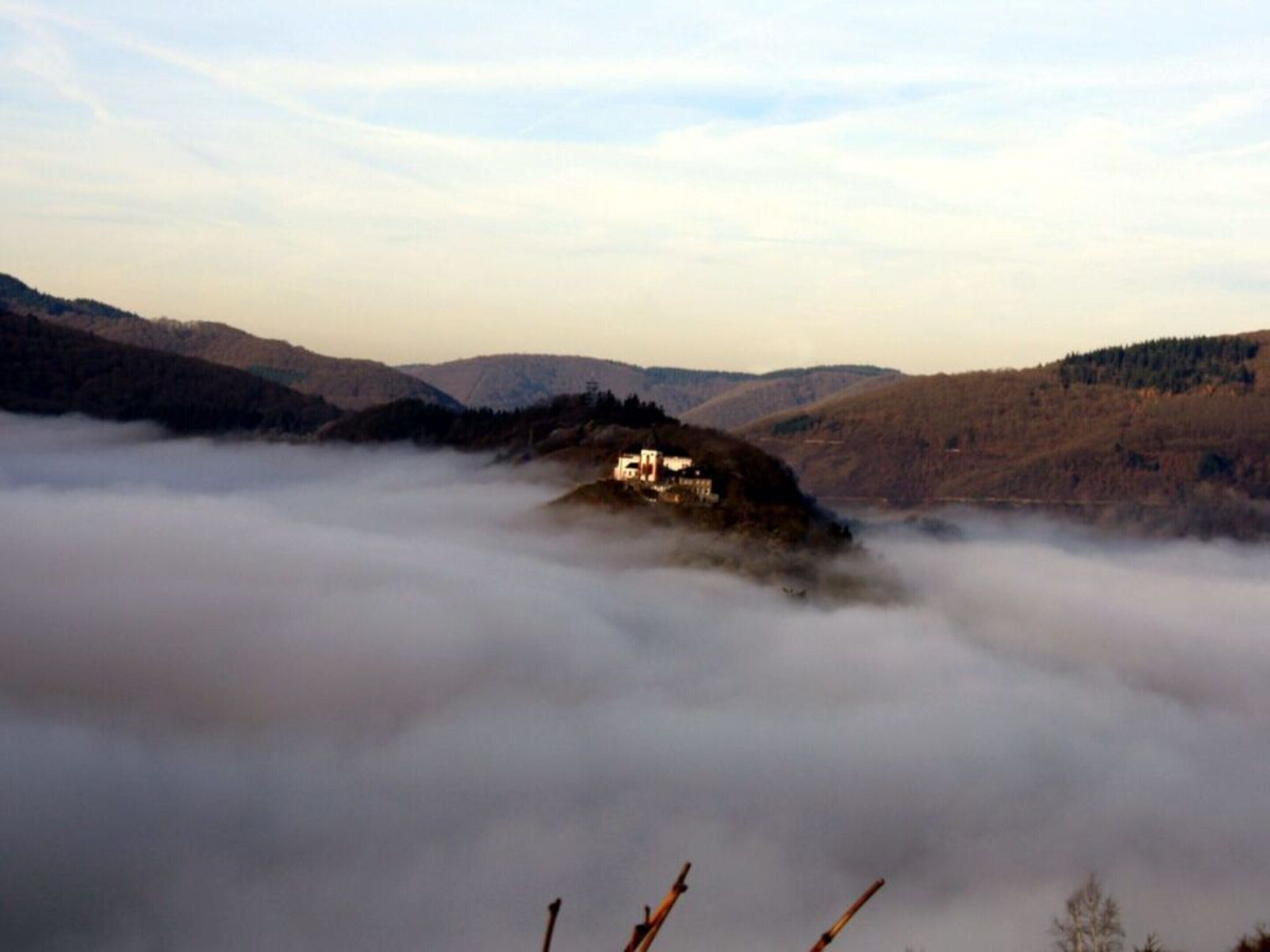A remote mountain lodge surrounded by fog, with a clear view of the surrounding hills.