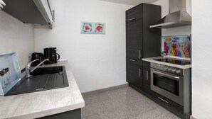 A compact kitchen with a sink, coffee maker, dark cabinets, and a colorful mural. - Tranquil Apartment in Zell-kaimt (Zell (Mosel))