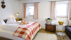 A bedroom with a bed, bedside tables, a nightstand, a lamp, a window with curtains, a small table with a plant and fruit bowl, and a sofa. - Farmhouse in Hollersbach Near Kitzski (Hollersbach im Pinzgau)