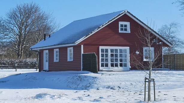 Ein rotes Holzhaus mit verschneietem Dach und weißer Tür.