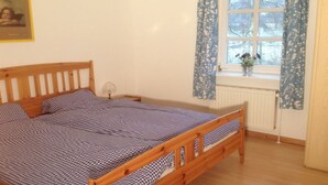 Ein Schlafzimmer mit einem hölzernen Bett, einem Nachttisch, einem Fenster mit Vorhängen und einer Heizung.