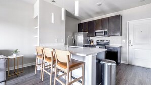 Une cuisine moderne dotée d’un îlot central, d’appareils électroménagers en acier inoxydable et de tabourets de bar en bois.